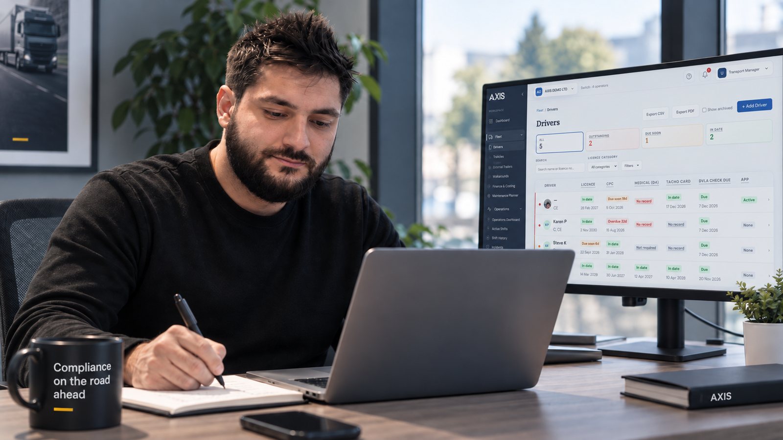 Catalin Budau at his desk, writing in a notebook, with the Axis Drivers screen for the AXIS DEMO LTD demo account open on the monitor behind him
